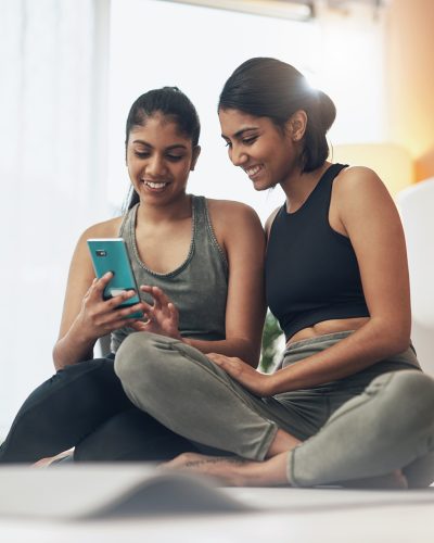 exercise-phone-women-together-home-floor-with-internet-social-media-app-indian-sisters-female-friends-lounge-with-smartphone-online-class-chat-fitness-workout-with-partner (1)